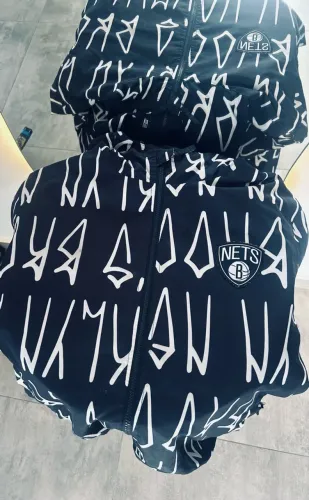 uma jaqueta corta-vento do Brooklyn Nets, da NBA, preta com estampa branca.