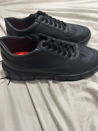 sapatênis preto de solado reto, com cadarços escuros e detalhe interno avermelhado.