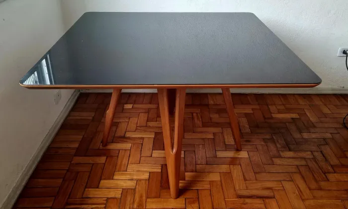 Mesa de jantar 120x120cm com estrutura em madeira e tampo de vidro preto.