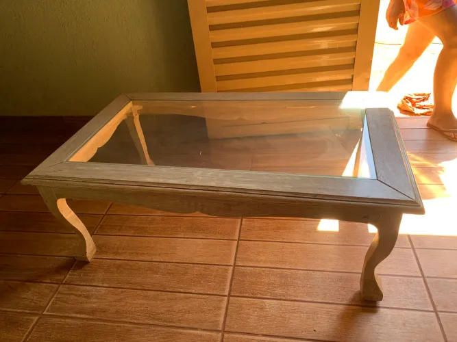 Esta é uma mesa de centro clássica de madeira com tampo de vidro e pés curvados.