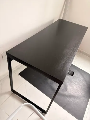 Mesa de escritório preta, espaçosa e com estrutura metálica.