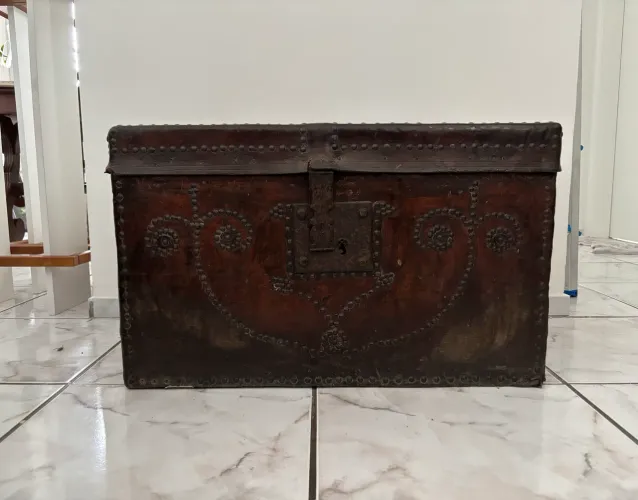Baú de couro com desenhos ornamentais de tachas metálicas.