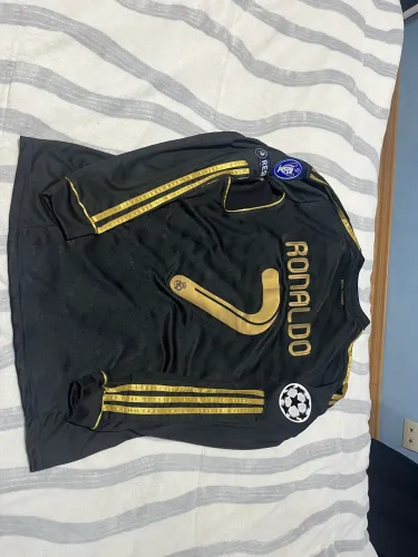 Camisa CR7 preta com detalhes em dourado, e patchs da época de real madrid