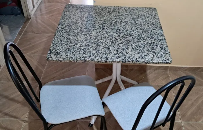 Mesa com tampo de pedra desmontável, com 2 cadeiras de tubo branca.