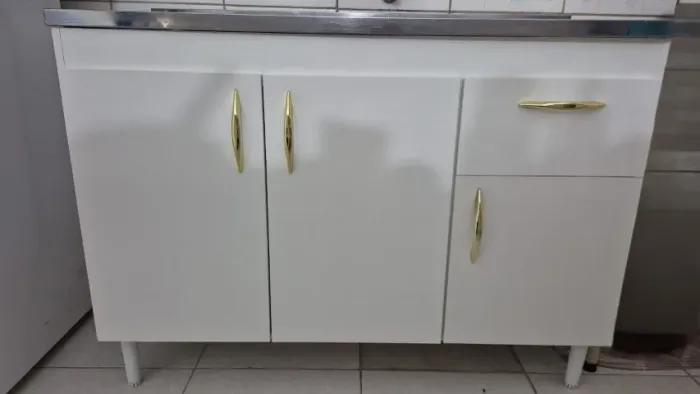 Balcão de pia branco com puxadores dourados e tampa de inox