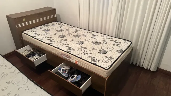 Cama de solteiro com baú na cabeceira, duas gavetas laterais e prateleiras laterais.