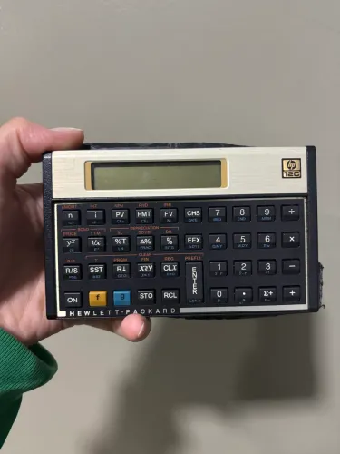 Calculadora Financeira HP 12C clássica com visor LCD e placa frontal dourada.