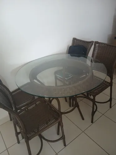 Mesa de vidro e fibra com 4 cadeiras, sendo que as cadeiras tem alguns detalhes.