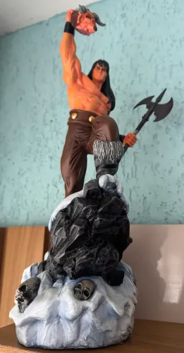 Estátua colecionável de Conan, o Bárbaro, posicionado sobre uma base rochosa com crânios