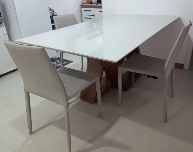 Mesa com tampa de vidro e 4 cadeiras, uma ponta rachada.