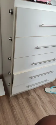 cômoda de madeira branca com cinco gavetas e puxadores metálicos horizontais,