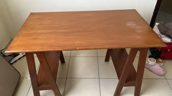 Mesa de madeira maciça, espaçosa, com espaço para colocar livros na parte inferior.