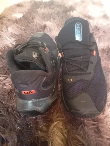 tênis de basquete  Under Armour Buzzer 2 preto com detalhes em laranja.