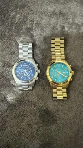 Relógios Michael Kors, grandes, um dourado com fundo esverdeado e prata com fundo marinho.