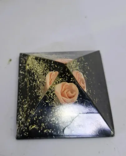 Orgonite feito de resina contendo partículas douradas e flores em tons de rosa.