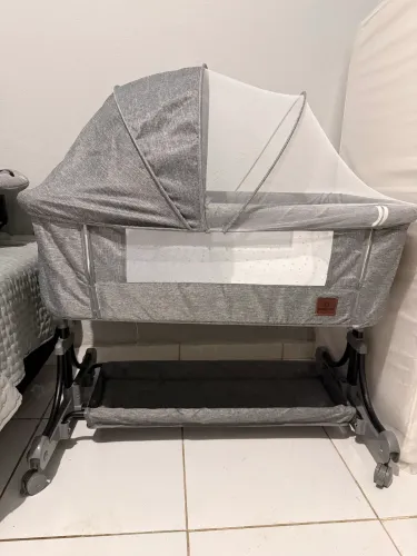Este berço portátil Bambinelli é um modelo Moisés cinza com mosquiteiro e função balanço.