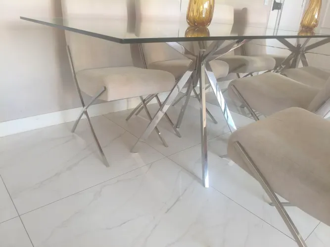 Mesa com base de inox com tampa de vidro, e quatro cadeiras.