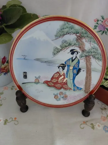 Prato em porcelana oriental com paisagem e gueixas. Filetes dourados em toda borda