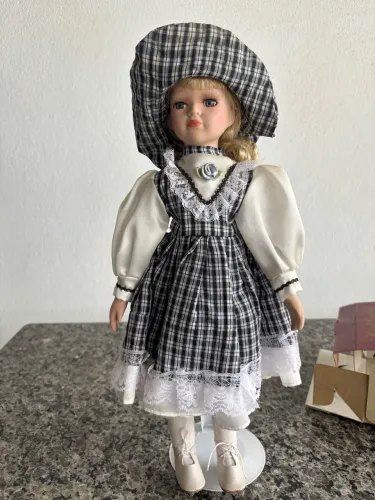 Boneca de porcelana estilo camponesa vintage com vestido xadrez preto e branco e chapéu.
