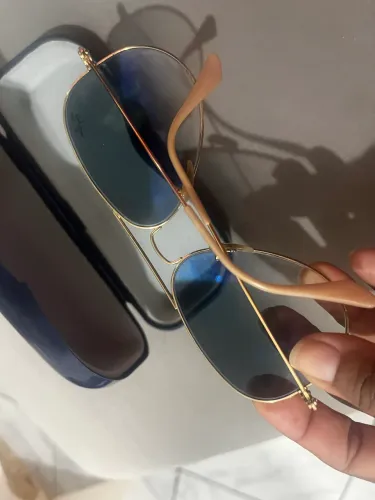 óculos de sol Ray-Ban Aviator possuem armação dourada e lentes azul degradê.