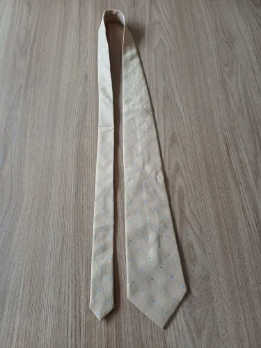 Gravata TNG dourada, com pontinhos branco e azul.