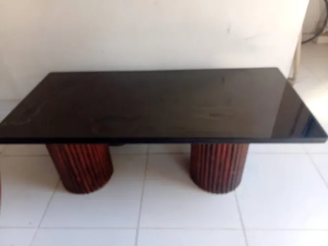 Mesa de centro com tampo de vidro preto, pés de madeira.