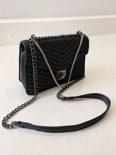 Bolsa feminina matelasse preta com adorno decorativo alça transversal, fecho imã e zíper 