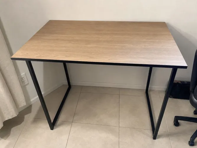 Mesa escrivaninha estilo industrial com tampo amadeirado e pés de metal preto.