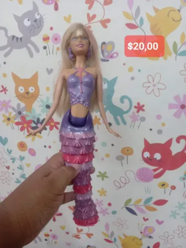 Barbie em Vida de Sereia", com cabelo loiro e cauda roxa e rosa com babados.