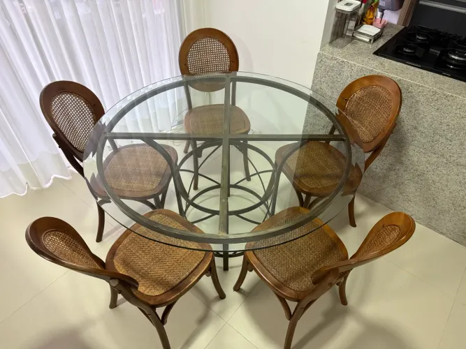 Mesa redonda de vidro com pé metálico, com 5 cadeiras de madeira com palha sextavada.