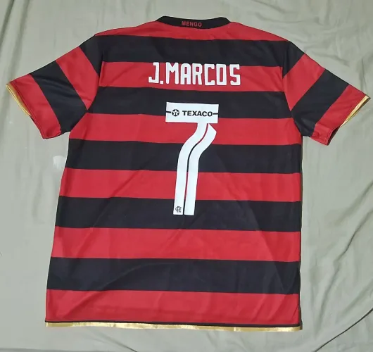 camisa do Flamengo título campeão de 2025 com detalhes em dourado nas golas/mangas. Usado