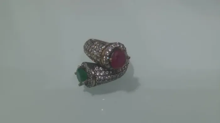 Anel de prata em forma tubular com pedras brilhantes e pedras vermelha e verde