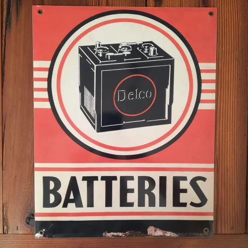 Placa de metal vintage apresenta uma estampa clássica de publicidade da Delco Batteries