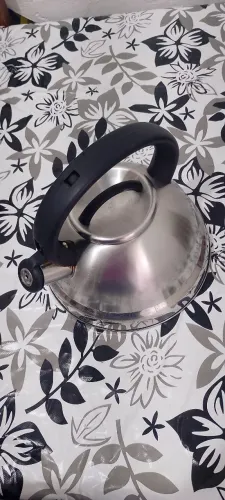chaleira de aço inoxidável com acabamento polido, alça preta e tampa com puxador.