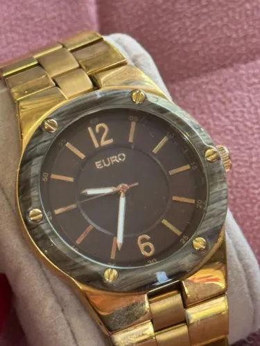 Relógio Euro em tom dourado com mostrador preto e aro com parafusos