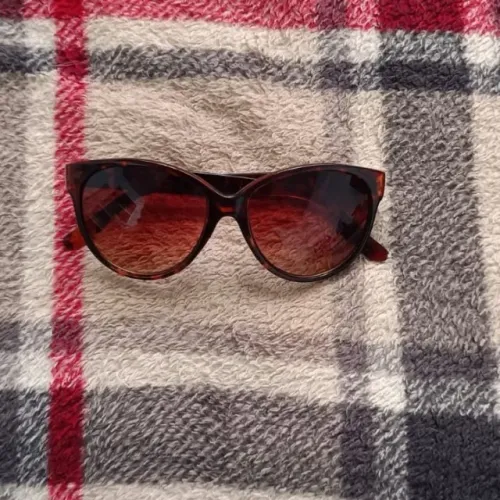 óculos de sol com armação marrom estilo tartaruga e lentes em tom avermelhado.