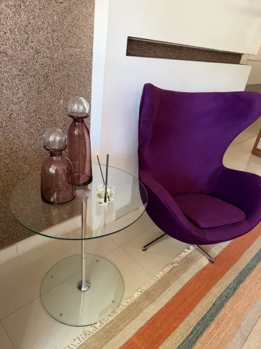 Mesa lateral com estrutura cromada e tampo em vidro, diâmetro 60cm e altura 67cm.