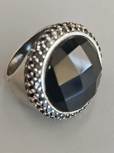 Anel de prata com uma pedra preta, possivelmente ônix, e detalhes cravejados.