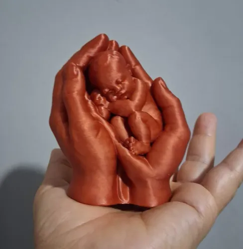 escultura mãos segurando bebê na cor cobre