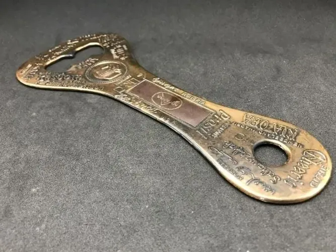 Antigo abridor gigante em metal, com diversas marcas de bebidas gravadas