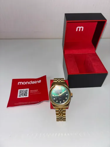 Relógio dourado fundo verde escuro Mondaine