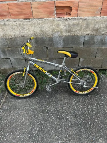 Esta é uma bicicleta infantil Aro 20 da marca Pro X, com um quadro cromado e amarelo