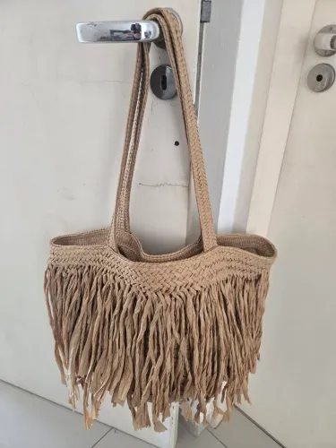 Bolsa de palha bege apresenta franjas longas e texturizadas na parte inferior.