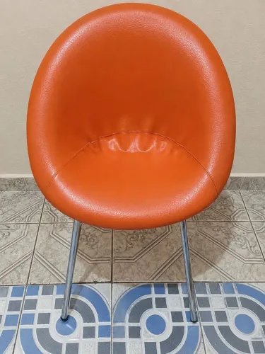 cadeira tipo concha, estofada em courino laranja, com pés de metal