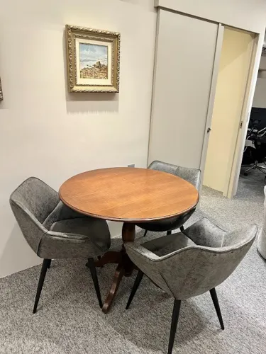 Mesa da Wood Prime em madeira redonda, com quatro cadeiras em couro sintetico cinza.