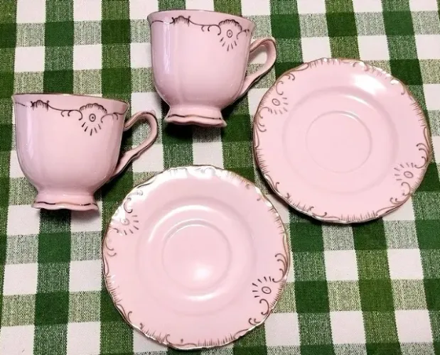 Par de xícaras de café rosa com detalhes dourados.