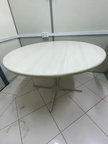 Mesa de jantar oval com tampo de madeira clara e base de metal cinza.