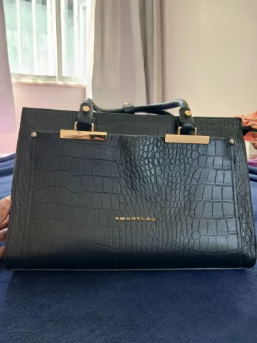 Bolsa grande preta com textura de couro de crocodilo com detalhes dourados