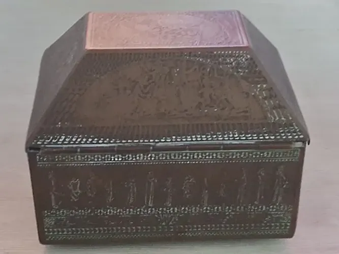 Porta joia de metal com desenhos históricos em volta da peça.