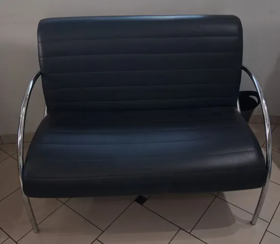 Sofá preta estilo "esteirinha" possui uma estrutura de metal cromado.